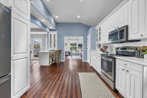 Kitchen with stainless steel appliances, glass insert cabinets, white cabinetry, light countertops, and backsplash