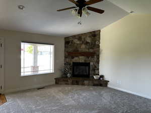 Unfurnished living room featuring ceiling fan, a stone fireplace, carpet flooring, baseboards, and lofted ceiling
