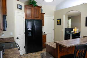 Kitchen with a peninsula, a breakfast bar, black appliances, arched walkways, and dark countertops