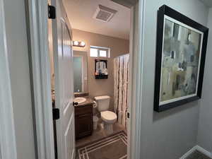 Full bathroom with toilet, a textured ceiling, visible vents, tile patterned flooring, and vanity