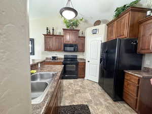 Kitchen with stone finish flooring, a sink, a textured ceiling, black appliances, and lofted ceiling