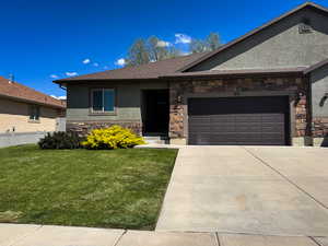 Ranch-style home with a garage, stucco siding, stone siding, and a front yard