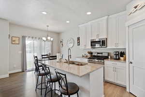 Kitchen with appliances with stainless steel finishes, a sink, light wood-style flooring, an island with sink, and recessed lighting