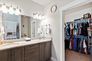 Full bath with a spacious closet, double vanity, and baseboards