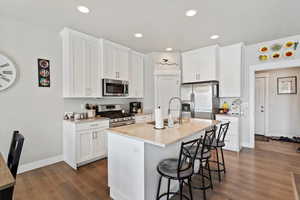 Kitchen with appliances with stainless steel finishes, a sink, dark wood-style flooring, a kitchen breakfast bar, and light stone countertops