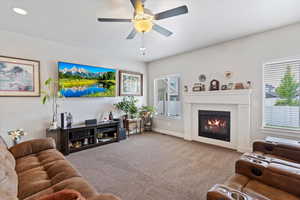 Carpeted living area with a glass covered fireplace, healthy amount of natural light, ceiling fan, and baseboards