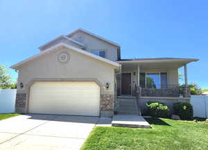 View of front of home featuring stone siding, an attached garage, covered porch, stucco siding, and concrete driveway