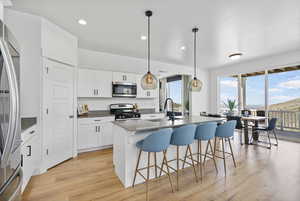 Kitchen featuring appliances with stainless steel finishes, a sink, recessed lighting, light wood finished floors, and a center island with sink