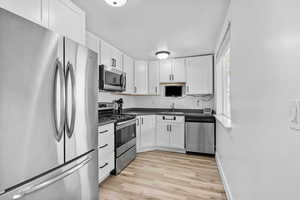 Kitchen featuring appliances with stainless steel finishes, a sink, dark countertops, and white cabinetry