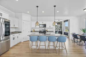 Kitchen featuring stainless steel appliances, recessed lighting, light wood-style floors, a kitchen breakfast bar, and white cabinetry