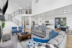 Living room featuring stairway, light wood-style flooring, a towering ceiling, and baseboards
