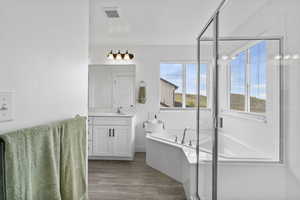 Full bathroom featuring vanity, wood finished floors, a garden tub, a shower stall, and baseboards
