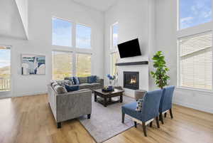 Living area featuring light wood-style floors, a high ceiling, a glass covered fireplace, and baseboards