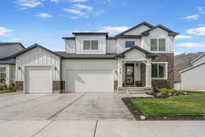 View of front of house with board and batten siding, stone siding, a front lawn, and driveway