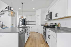 Kitchen featuring stainless steel appliances, dark countertops, light wood-style flooring, a sink, and recessed lighting