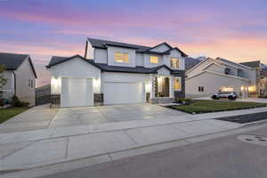 View of front facade featuring board and batten siding, stone siding, concrete driveway, a lawn, and an attached garage