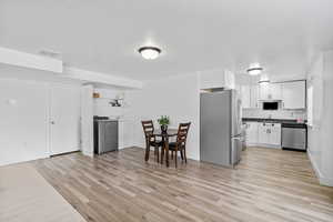 Kitchen featuring stainless steel appliances, washer / clothes dryer, light wood-style flooring, white cabinets, and a textured ceiling