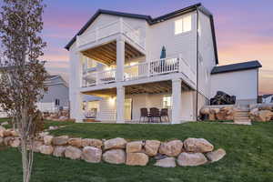 Back of house at dusk featuring a balcony, a patio, and a yard