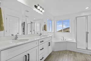 Bathroom with a stall shower, wood finished floors, double vanity, a garden tub, and recessed lighting