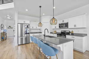 Kitchen featuring appliances with stainless steel finishes, a sink, dark countertops, light wood finished floors, and recessed lighting
