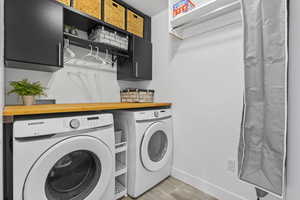 Laundry room with washing machine and clothes dryer, cabinet space, light wood-style floors, and baseboards