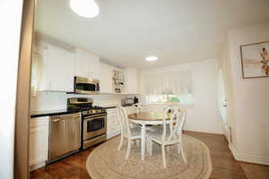 Kitchen with appliances with stainless steel finishes, white cabinets, tasteful backsplash, dark wood finished floors, and open shelves