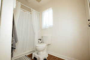 Bathroom with wood finished floors, baseboards, toilet, and a shower with curtain