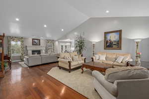 Living area with dark wood-type flooring, vaulted ceiling, recessed lighting, a glass covered fireplace, and baseboards