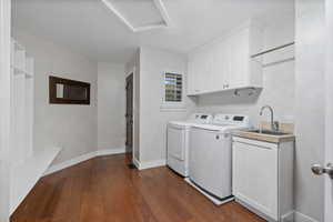 Clothes washing area featuring washing machine and dryer, dark wood-type flooring, cabinet space, attic access, and baseboards