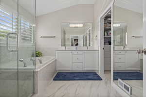 Full bathroom featuring lofted ceiling, marble look tiles, a bath, two vanities, and an enclosed shower