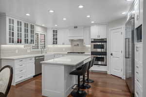 Kitchen with stainless steel appliances, a breakfast bar area, dark wood finished floors, tasteful backsplash, and recessed lighting