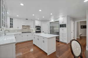 Kitchen featuring built in appliances, decorative backsplash, dark wood finished floors, light countertops, and a center island