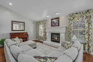 Living room featuring vaulted ceiling, a glass covered fireplace, wood finished floors, baseboards, and recessed lighting