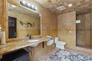 Bathroom featuring tile walls, toilet, and a sink