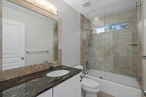 Bathroom with toilet, combined bath / shower with glass door, and vanity
