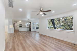 Unfurnished living room with light wood finished floors, baseboards, a ceiling fan, and visible vents