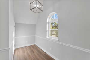 Interior space featuring baseboards, vaulted ceiling, a notable chandelier, and wood finished floors