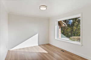 Unfurnished room featuring crown molding, wood finished floors, visible vents, and baseboards