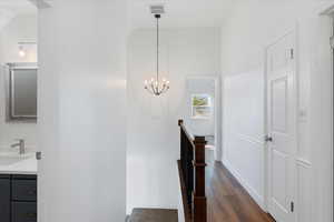 Staircase with an inviting chandelier, wood finished floors, high vaulted ceiling, visible vents, and baseboards