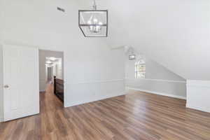 Additional living space featuring a notable chandelier, baseboards, visible vents, and wood finished floors