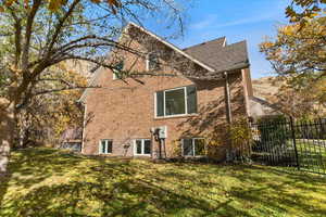 Rear view of house featuring a shingled roof, brick siding, fence, and a lawn