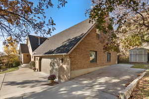 View of property exterior with roof with shingles, brick siding, concrete driveway, a garage, and a shed