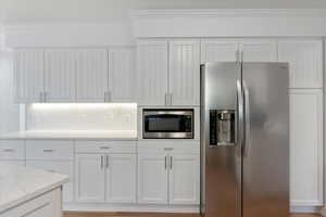 Kitchen with tasteful backsplash, ornamental molding, light stone counters, white cabinets, and appliances with stainless steel finishes