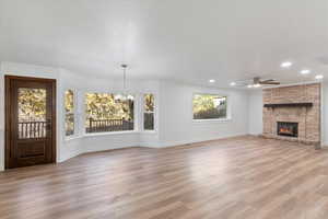 Unfurnished living room featuring light wood-style flooring, recessed lighting, baseboards, ceiling fan with notable chandelier, and a fireplace