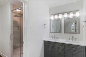 Bathroom featuring a shower stall, double vanity, and a sink
