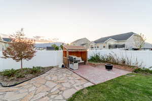 Patio terrace at dusk with a fenced backyard, a storage shed, and an outbuilding
