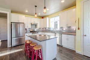 Kitchen with appliances with stainless steel finishes, white cabinetry, a sink, under cabinet range hood, and dark wood finished floors