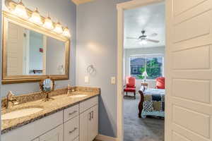 Ensuite bathroom featuring double vanity, baseboards, and a ceiling fan