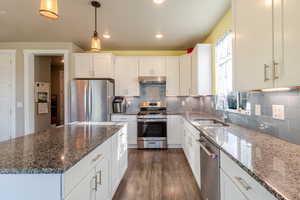 Kitchen with stainless steel appliances, a sink, dark wood-type flooring, under cabinet range hood, and white cabinets