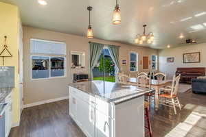 Kitchen featuring stainless steel microwave, a center island, dark wood finished floors, pendant lighting, and white cabinetry